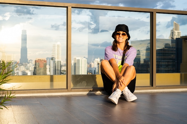 Free photo stylish caucasian woman in trendy panama and waist neon bag on roof in bangkok