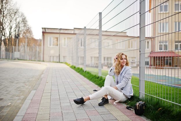 Stylish curly blonde model girl wear on white posing against fence