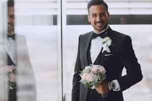 Free photo the stylish and elegant bridegroom is in the hotel room with a bouquet of flowers