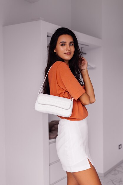 Stylish fashion young caucasian woman blogger at home in bedroom wearing brick color shirt and skirt