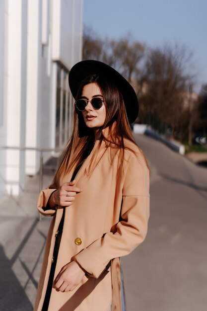 Stylish fashionable woman in black hat standing and posing outdoors.