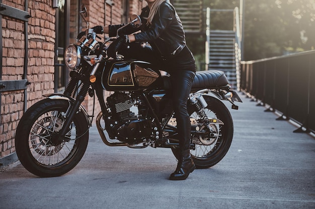 Free photo stylish female biker is sitting at her black bike while posing for a photoshoot on the street.