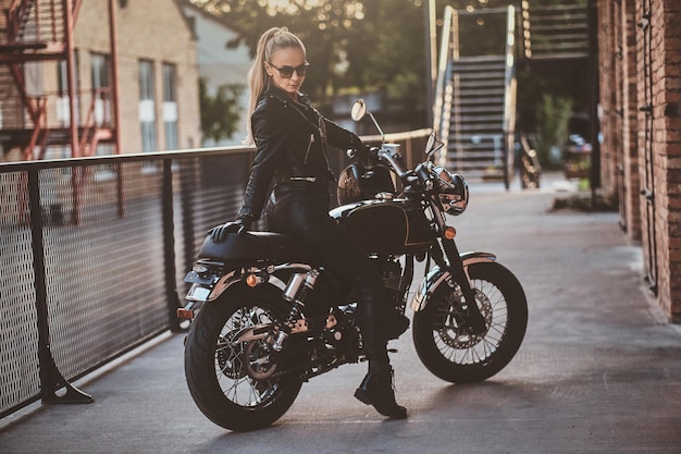 Free Photo stylish female biker is sitting at her black bike while posing for a photoshoot on the street.