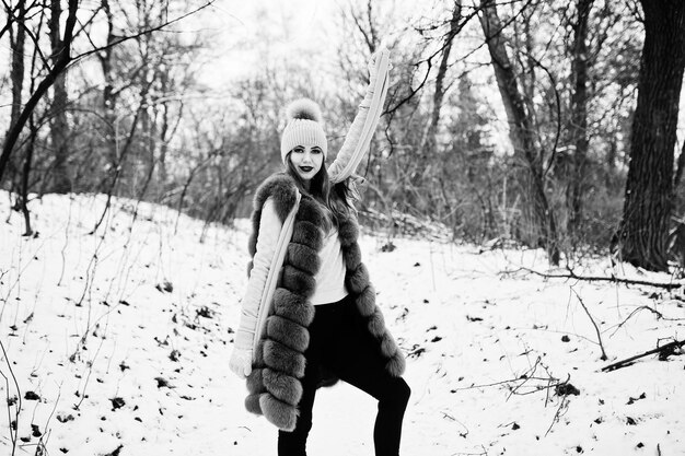 Stylish girl in fur coat and headwear at winter forest