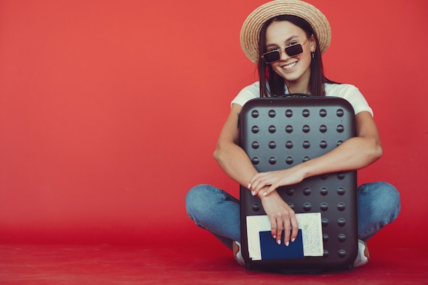 Free photo stylish girl posing with travel equipment on a red wall