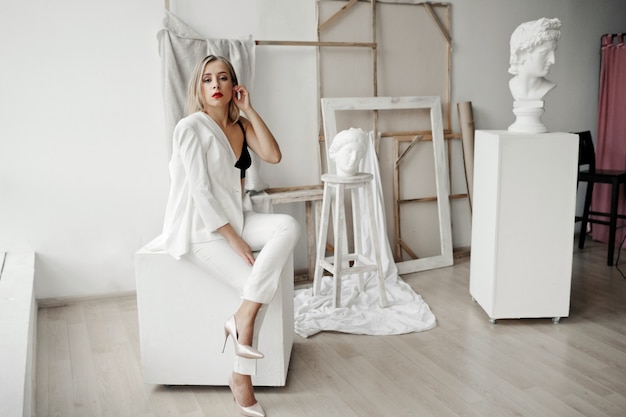 Free Photo stylish girl in a white suit sits on a white cube in a gallery