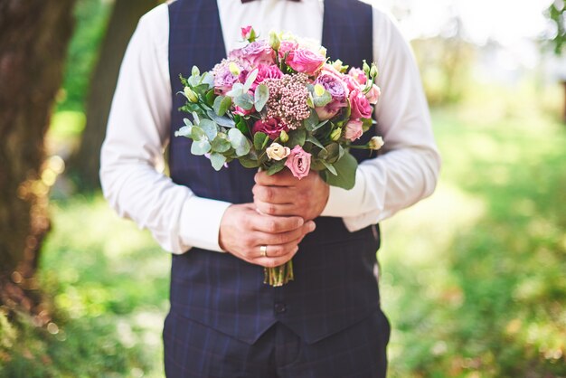 Stylish groom holding a tender pink wedding bouquet.