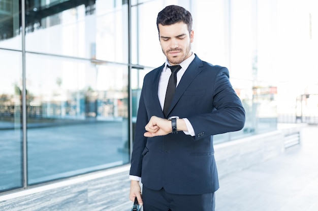 Stylish and handsome Latin businessman checking the time on his watch in city