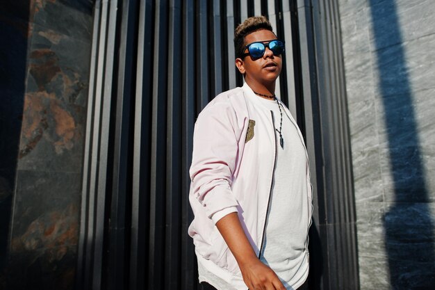 Stylish hipster arab man guy in sunglasses posed outdoor in street at sunset against gray wall