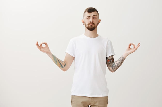 Free Photo stylish hipster guy trying meditate, peeking left at bothering sound