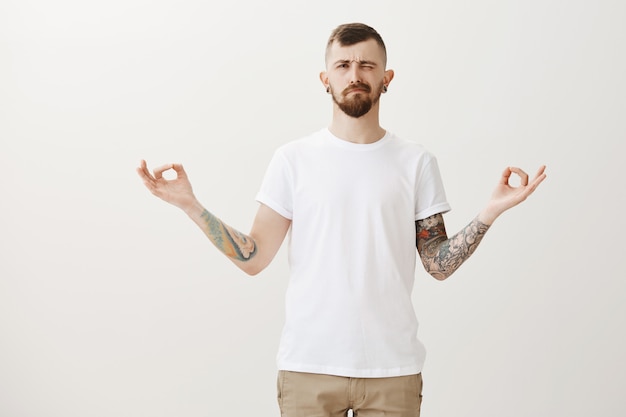 Free Photo stylish hipster guy trying meditate, peeking left at bothering sound