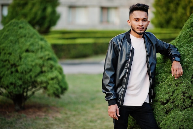 Stylish indian beard man at black leather jacket India model posed at green garden of city