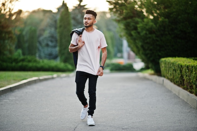 Stylish indian beard man at pink tshirt with black leather jacket on the shoulder India model walking at evening city