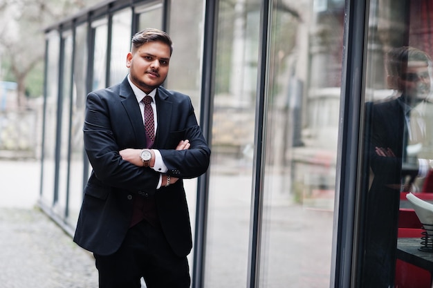 Free photo stylish indian businessman in formal wear standing against windows in business center