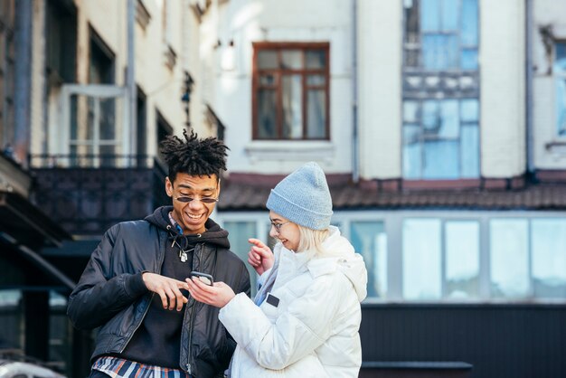 Stylish interracial teenage couple making fun by looking on mobile phone