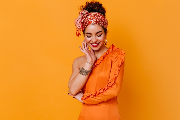 Free Photo stylish lady in orange dress and bright bandage on her head with shy smile looks down on orange space.