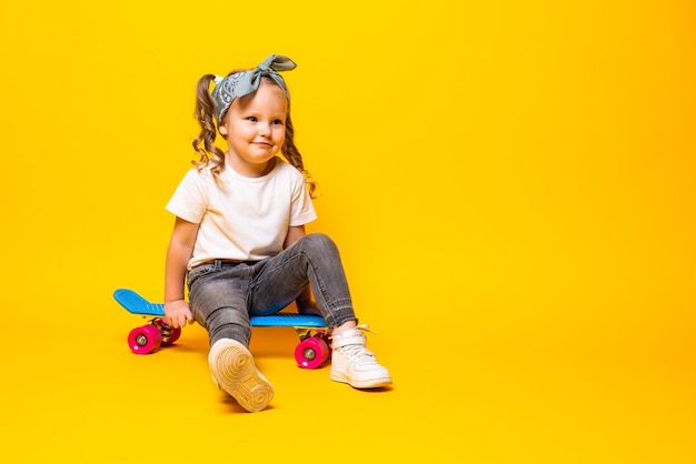 Stylish little girl child girl in casual with skateboard over yellow wall.