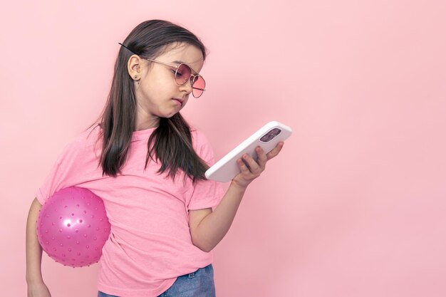 Stylish little girl with a smartphone on a pink background