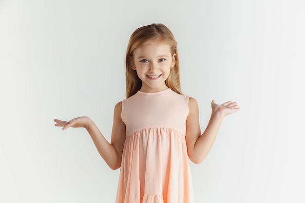 Stylish little smiling girl posing in dress isolated on white wall. Caucasian blonde female model. Human emotions, facial expression, childhood. Smiling, astonished, wondered.