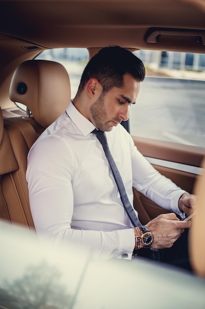 Free photo stylish male in a white shirt using smartphone in a luxury car.