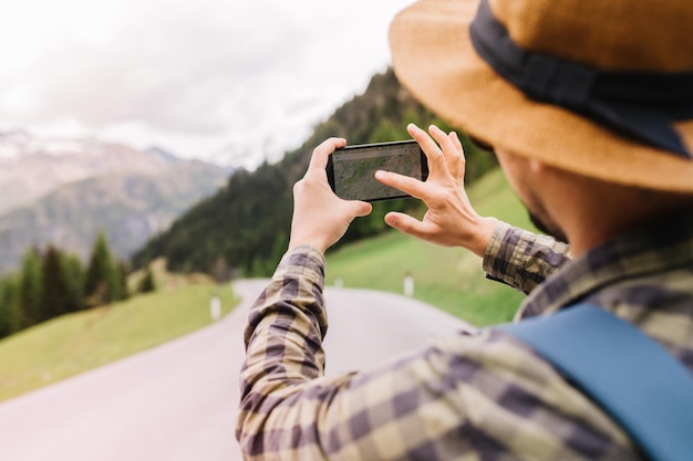 Free photo stylish man has lost his way and looking for new route on map in the phone walking down the road. outdoor portrait from back of traveler in checkered shirt going to mountains in vacation.