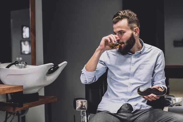 Free photo stylish man having drink in barbershop