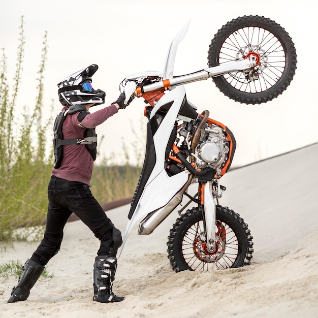 Free photo stylish man raising motorbike in the desert