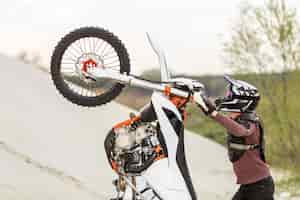 Free photo stylish man raising motorbike in the desert