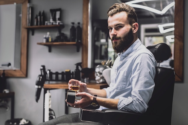 Stylish man with alcohol drink in barbershop