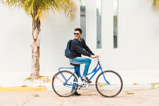 Stylish man with his backpack riding on blue bicycle