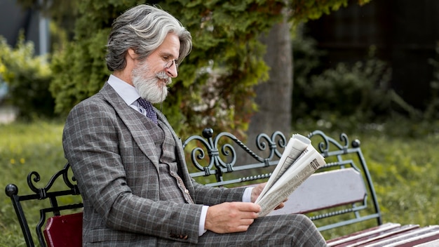 Stylish mature male reading newspaper outdoors