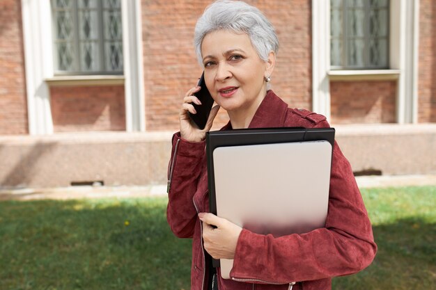 Stylish middle aged businesswoman using mobile to call taxi