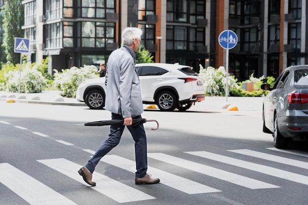 Stylish older man in the city crossing the street while holding umbrella