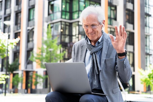 Stylish older man in the city using laptop for video call