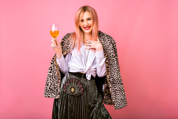 Free photo stylish positive pretty young woman having fun, wearing evening sparkling cocktail outfit and fur leopard printed trendy coat, pink background, enjoying winter holidays party.