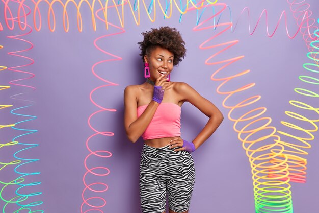 Stylish positive slim woman looks aside with smile, wears crop top and zebra leggings, being in good mood