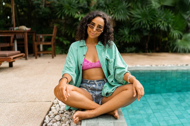 Free photo stylish pretty girl in summer outfit sitting near pool  vacation and travel mood bright colors trendy accesorises