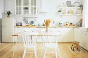 Free photo stylish scandinavian kitchen interior: chairs and table in foreground, fridge, long wooden counter with machines, utensils on shelves. interiors, design, ideas, home and coziness concept