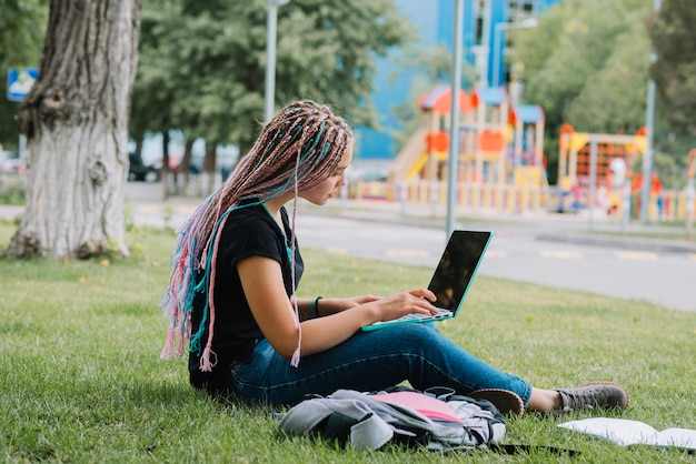 Stylish schoolgirl in park with laptop