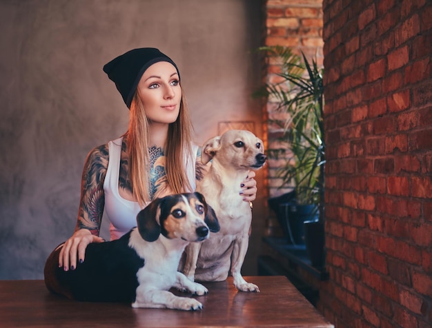 Free photo a stylish tattoed blonde female in t-shirt and jeans embraces two cute dogs.