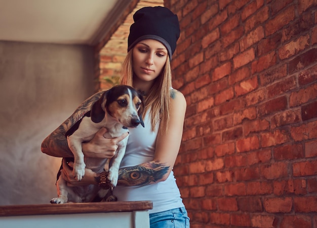 Free photo a stylish tattoed blonde female in t-shirt and jeans holds a cute dog.