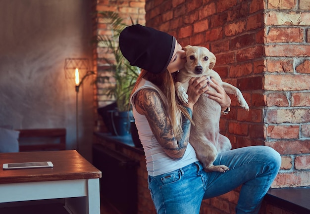 Free photo a stylish tattoed blonde female in t-shirt and jeans holds a cute dog.