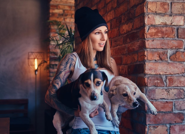 Free photo a stylish tattoed blonde female in t-shirt and jeans holds two cute dogs.