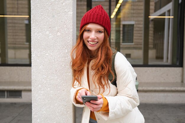 Stylish urban girl using mobile phone app standing in city waiting for taxi looking at smartphone ap