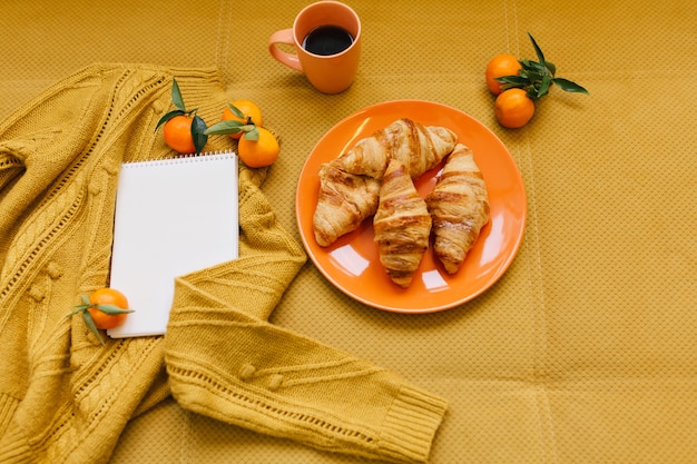 Free photo stylish winter image in orange colors from above of knitted sweater, croissants, clementines and notebook on table