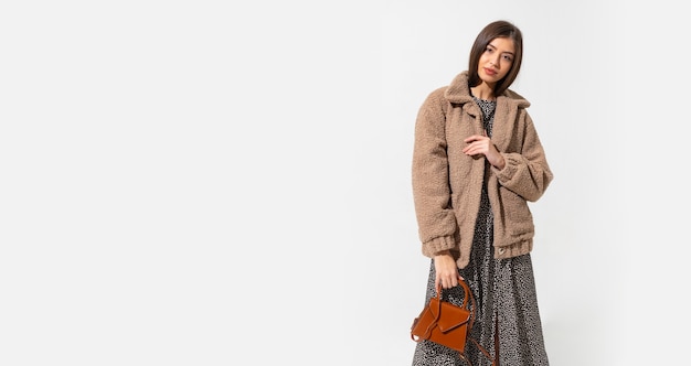 Stylish woman in beige fur coat and dress posing.