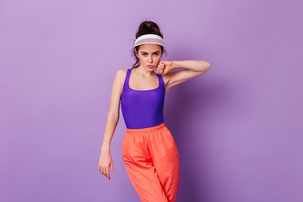 Free photo stylish woman in cap and outfits from 80s posing on purple wall