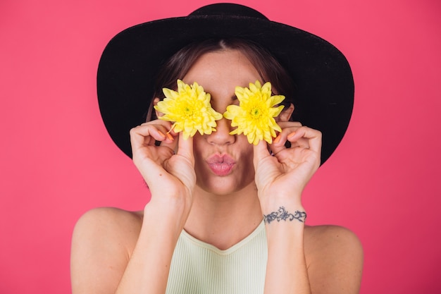 Free photo stylish woman in hat, send air kiss cover eyes with yellow asters, spring mood, happy emotions isolated space