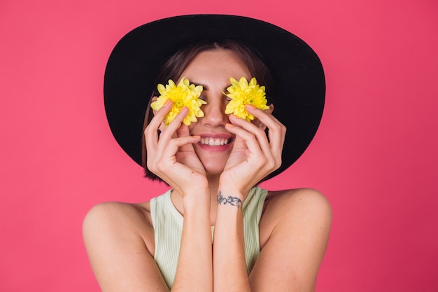 Free photo stylish woman in hat, smile on face cover eyes with yellow asters, spring mood, happy emotions isolated space