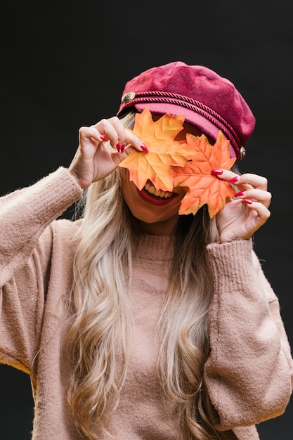 Free photo stylish woman hiding her face behind dry maple leaves against black background